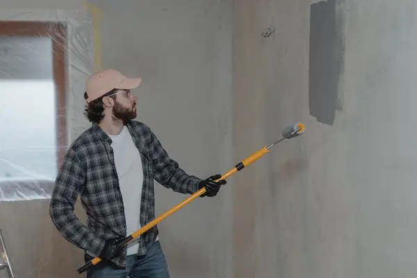 Painter rolling grey paint onto an interior wall in Greensboro